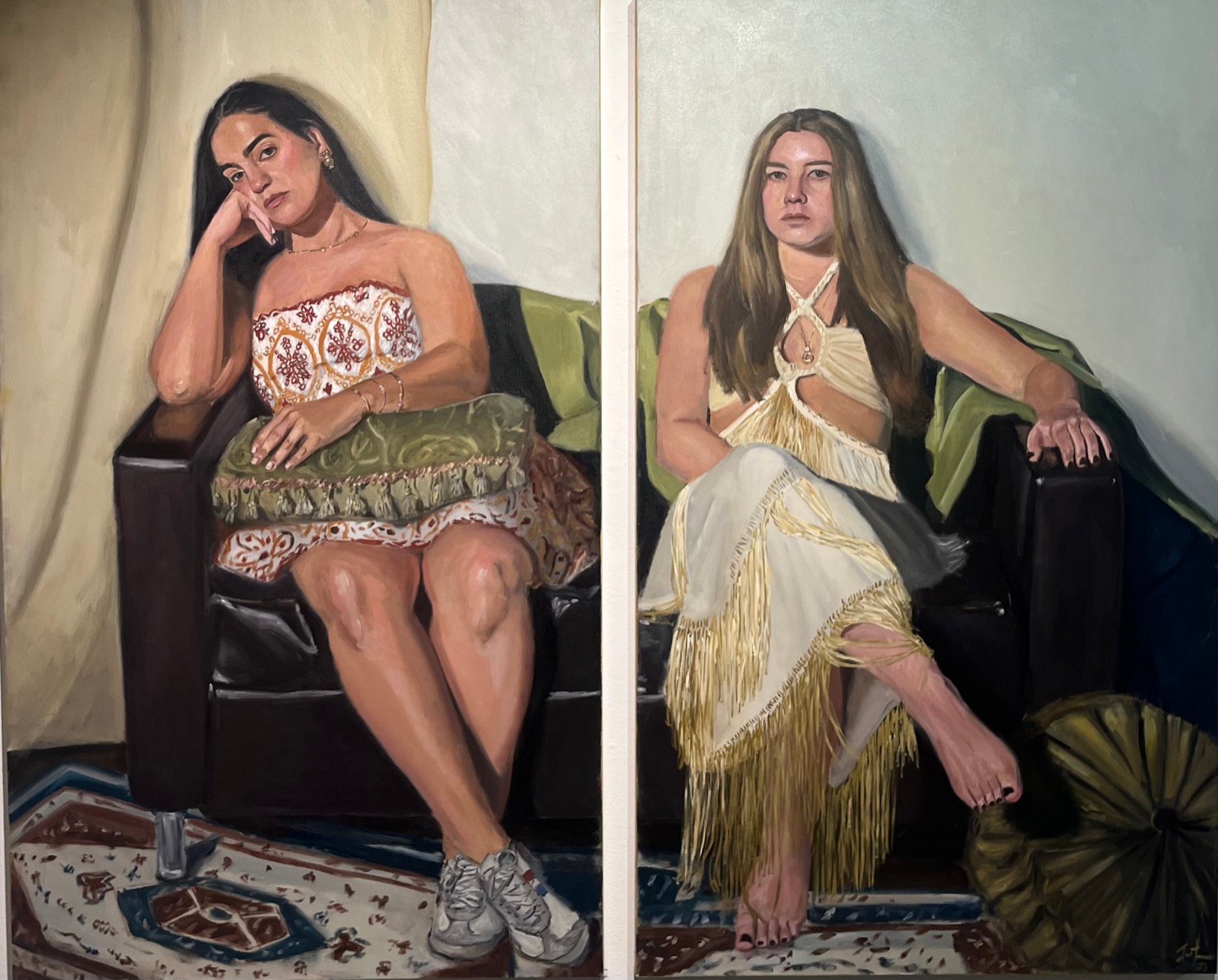 Diptych of two young women seated on a dark sofa draped with green fabric, one in an embroidered white top and sneakers, the other in a fringed cream dress, above a patterned rug